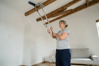 Femme utilisant un balai télescopique pour nettoyer un plafond en hauteur dans un salon moderne