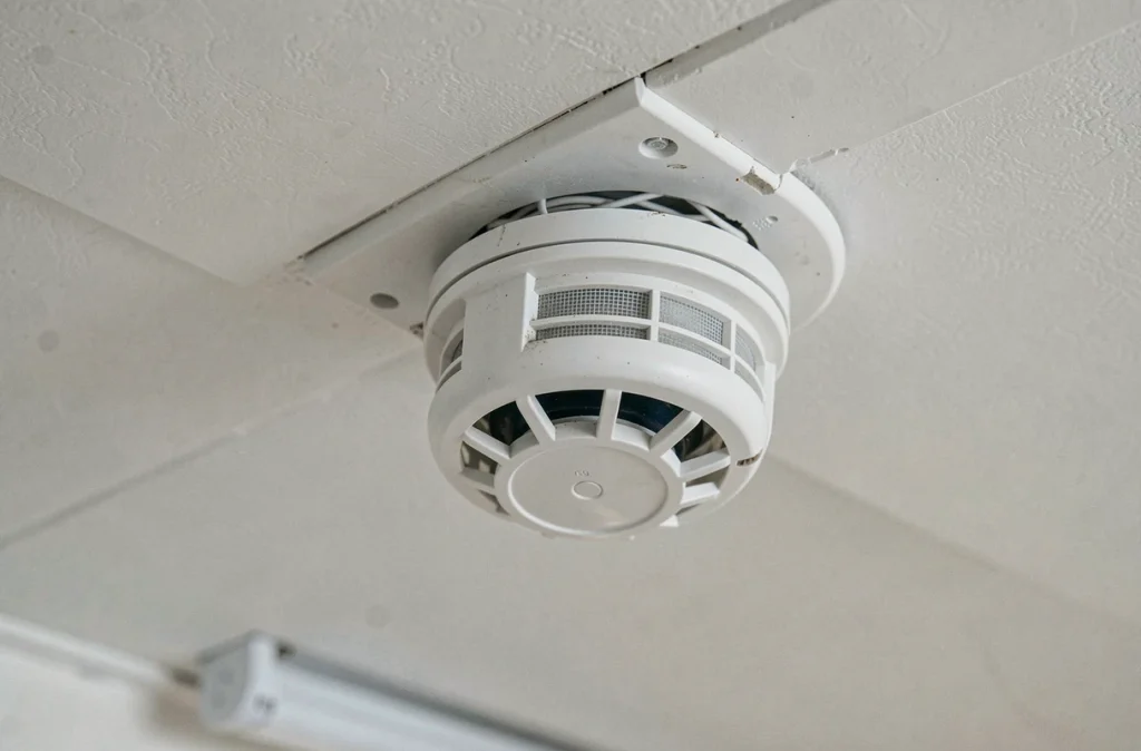 Détecteur de fumée mal installé dans un coin de plafond avec câblage mal positionné et fixation incorrecte