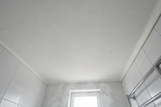 Plafond en toile tendue dans une salle de bains moderne vue en contre-plongée, montrant la texture du tissu blanc mat au-dessus des carreaux de céramique